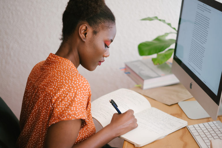 A woman using freelance tools to write in a notebook on her desk.