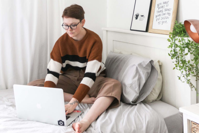 a person sitting on a bed with a laptop.