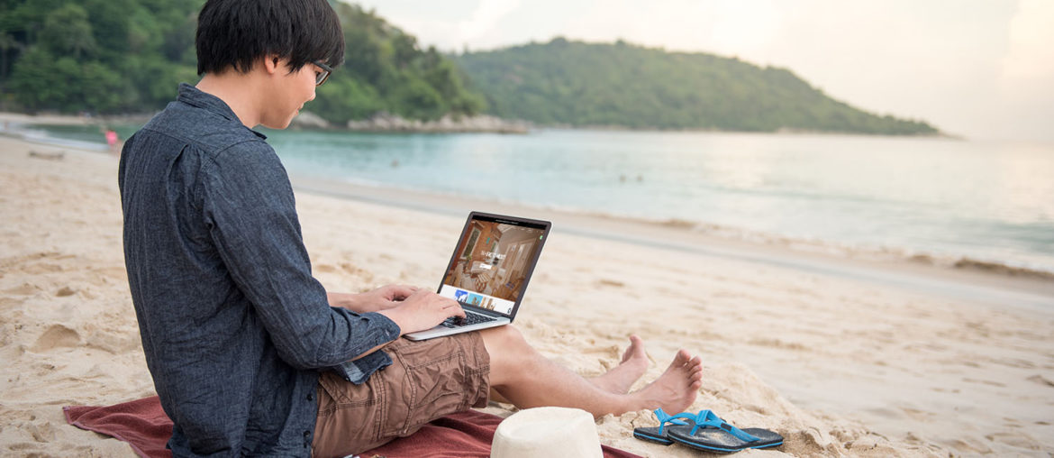 A digital nomad on a beach using a laptop computer.