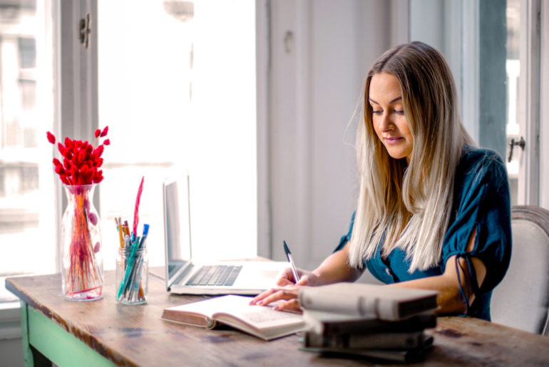 a woman sitting at a table with a book and a laptop.