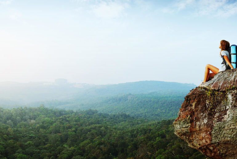 A person practicing slow travel sitting on top of a cliff.