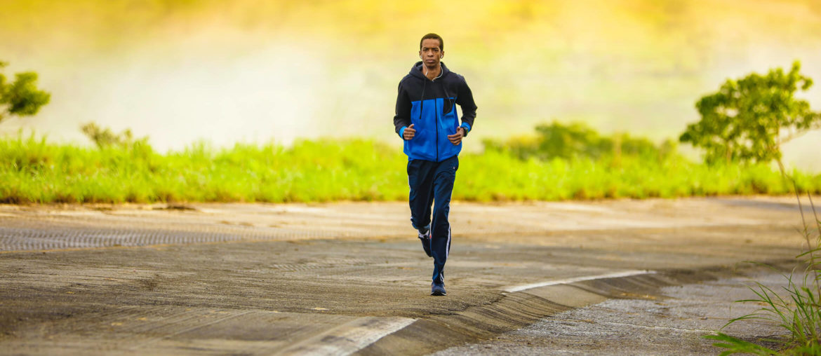 A fitness enthusiast running down a road in a blue jacket.