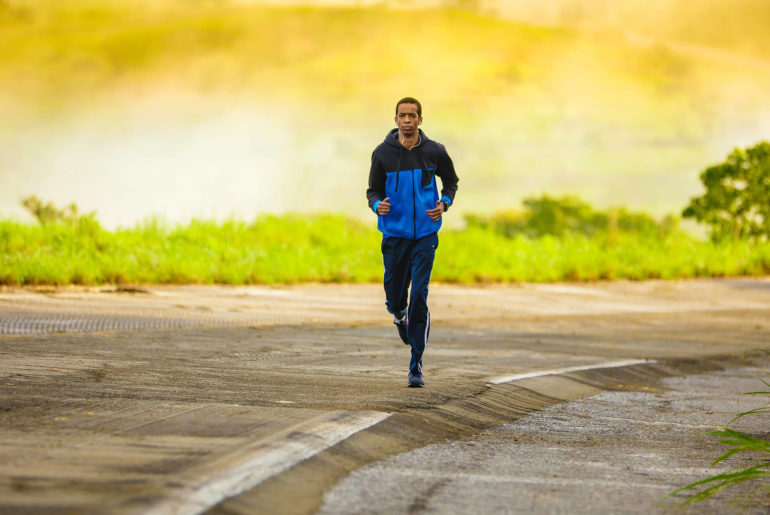 A fitness enthusiast running down a road in a blue jacket.