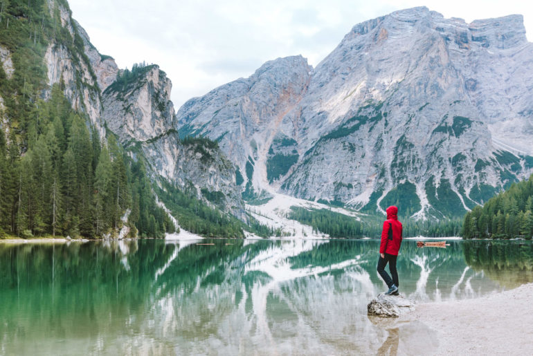 a person standing on a rock in front of a mountain lake.