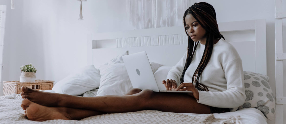 a woman sitting on a bed using a laptop computer.