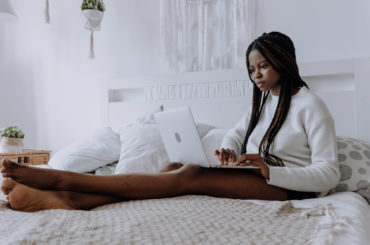 a woman sitting on a bed using a laptop computer.