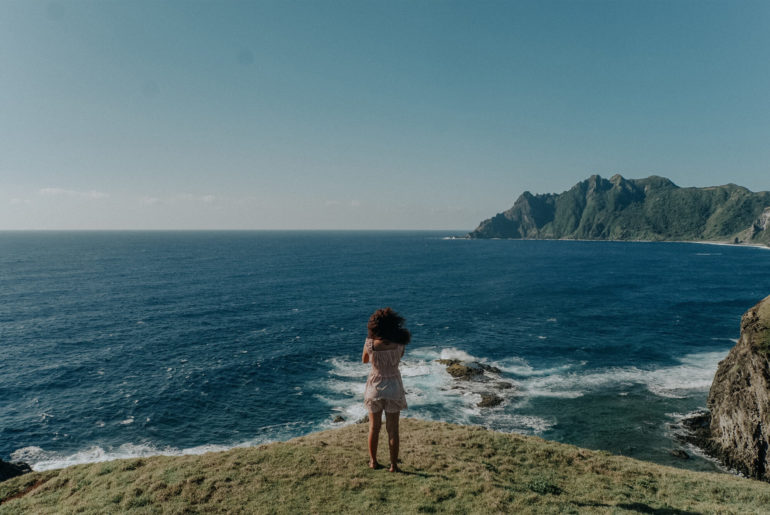 A digital nomad enjoying the Philippines, standing on top of a lush green hillside next to the ocean.