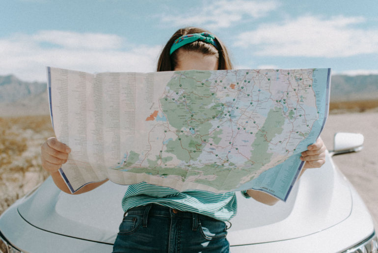 a woman holding a map in front of a car.