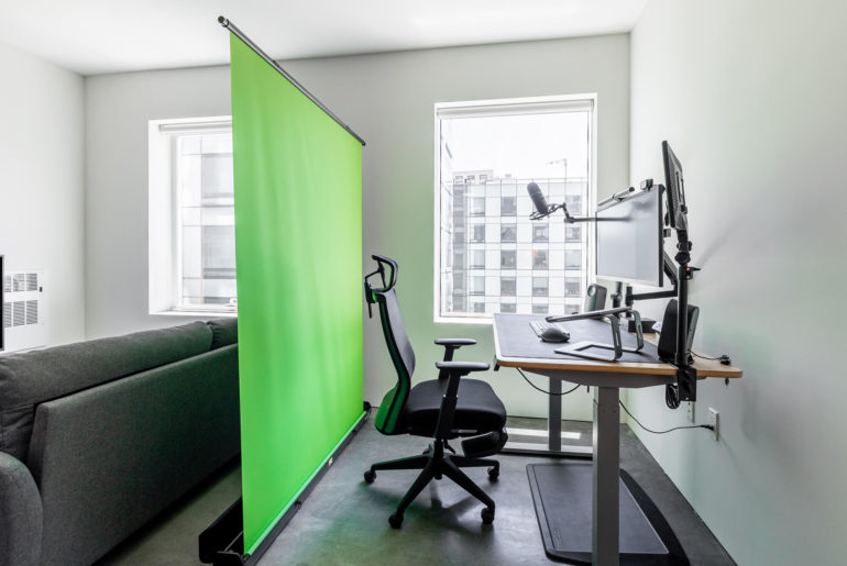 A rental living room with a green screen in the corner for remote work.