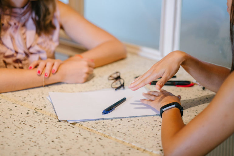 Two women writing about how to put remote work on the resume at a table.