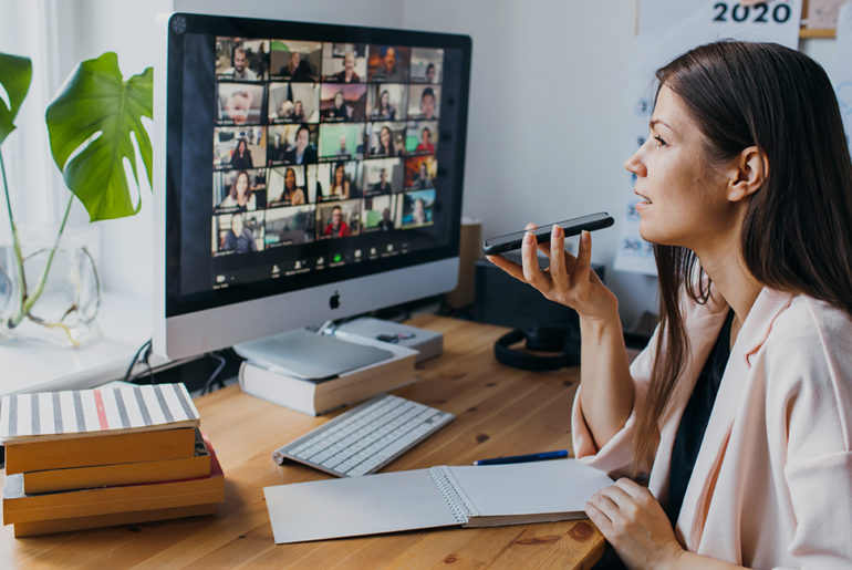 A woman managing a remote team sits at her computer with a pen in hand.