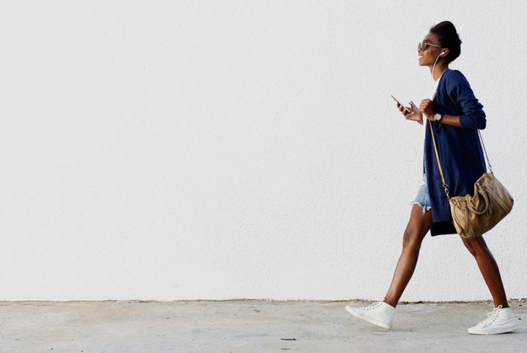 A woman finding stress relief while walking down a street with a cell phone in hand.