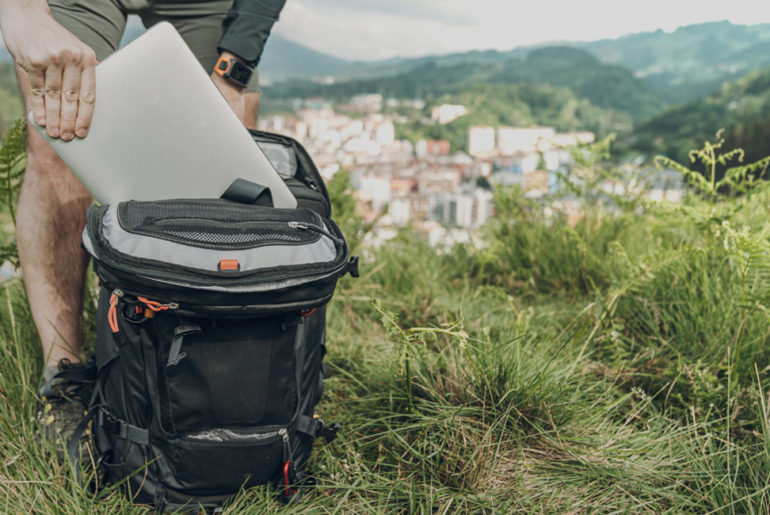 A man on a workation with a laptop and backpack in the grass.