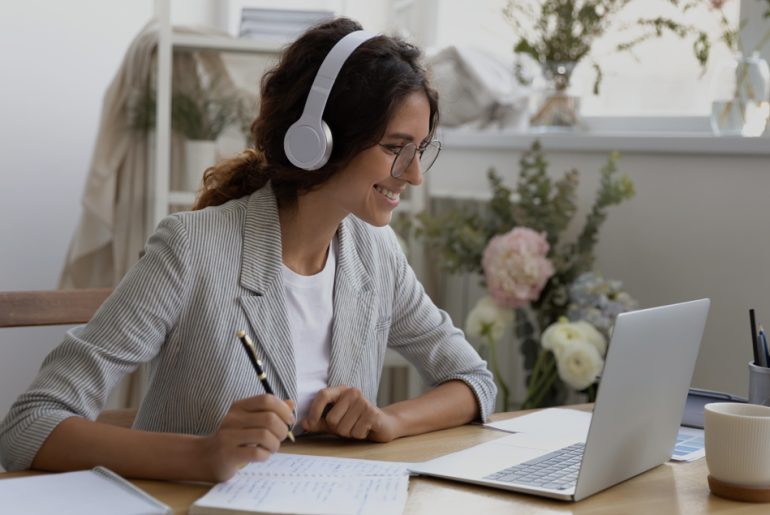 A woman participating in a virtual meeting with a laptop and headphones on at a table.