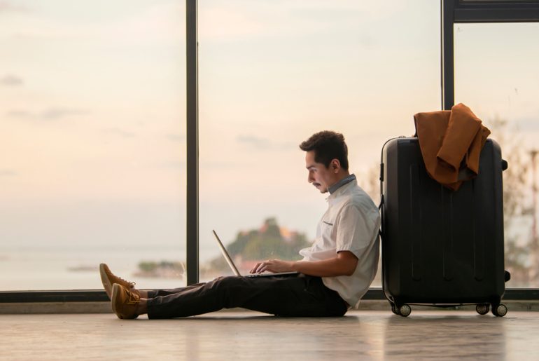 A man is using a laptop to work remotely while sitting on the floor.
