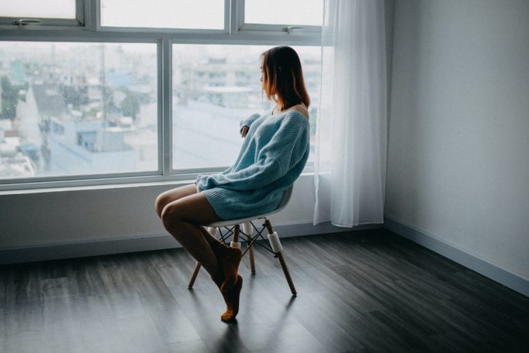 A woman sitting in a chair looking out a window after relocation.