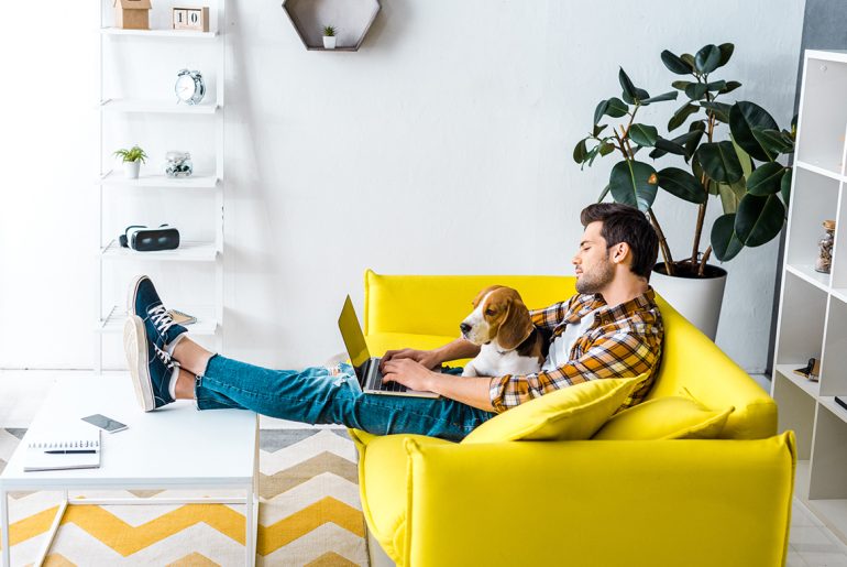 A man on a yellow couch enjoying the benefits of pet ownership with his dog on his lap.