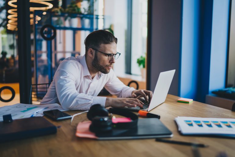A man engaged in remote work sitting at a table with his laptop.