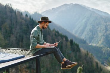 A man using his travel credit to sit on a bench and look at his cell phone.