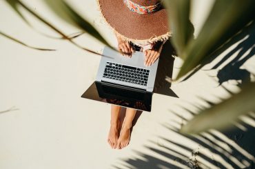 A remote worker wearing a floppy hat typing on her laptop.