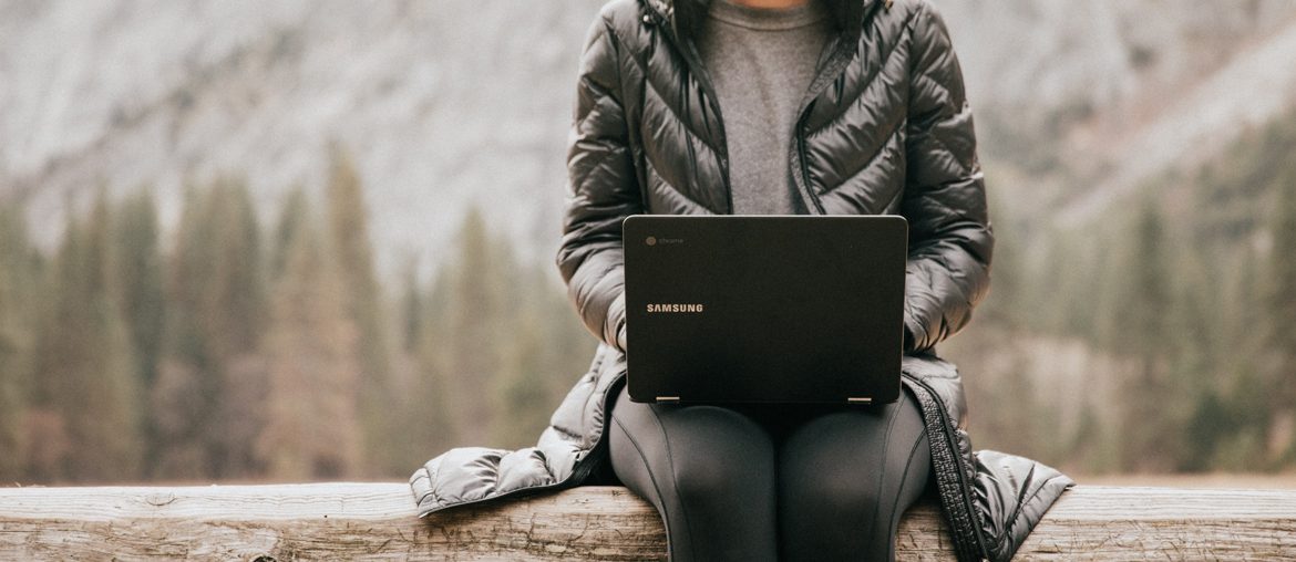 A woman sitting on a log using a laptop, motivated.