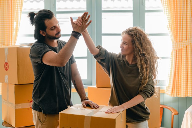 A man and a woman standing next to each other in front of boxes while engaged in remote work.