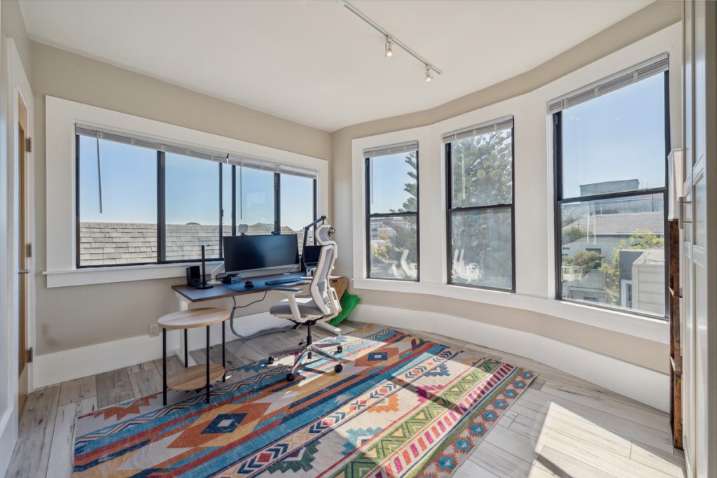 A room with a rug, a desk, and three windows for jobs that require travel.