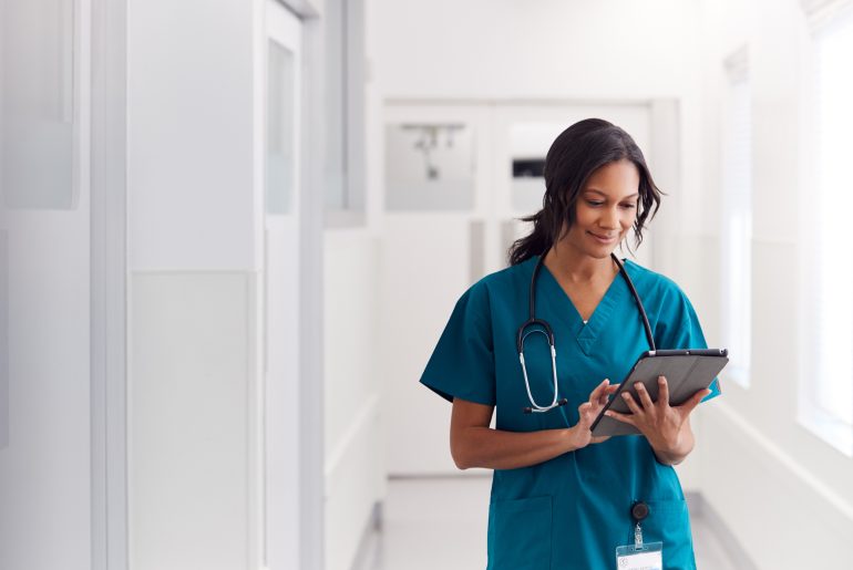A travel nurse in scrubs is looking at a tablet.