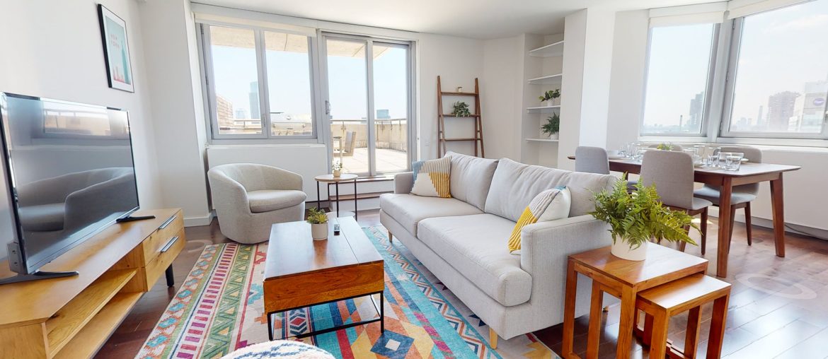 A living room with large windows and a colorful rug available for subletting.