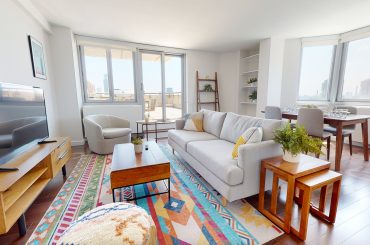 A living room with large windows and a colorful rug available for subletting.