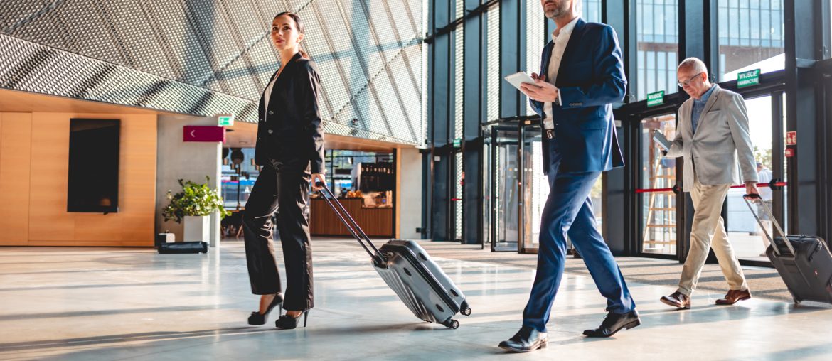 A group of executive business people walking through a lobby with luggage.