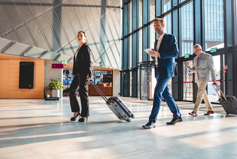 A group of executive business people walking through a lobby with luggage.