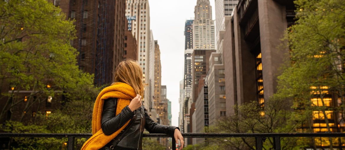 A woman wearing an orange scarf is standing on a railing in new york city.