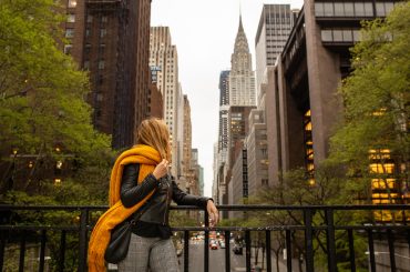 A woman wearing an orange scarf is standing on a railing in new york city.