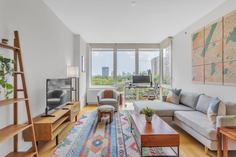 A furnished living room with large windows and a rug.