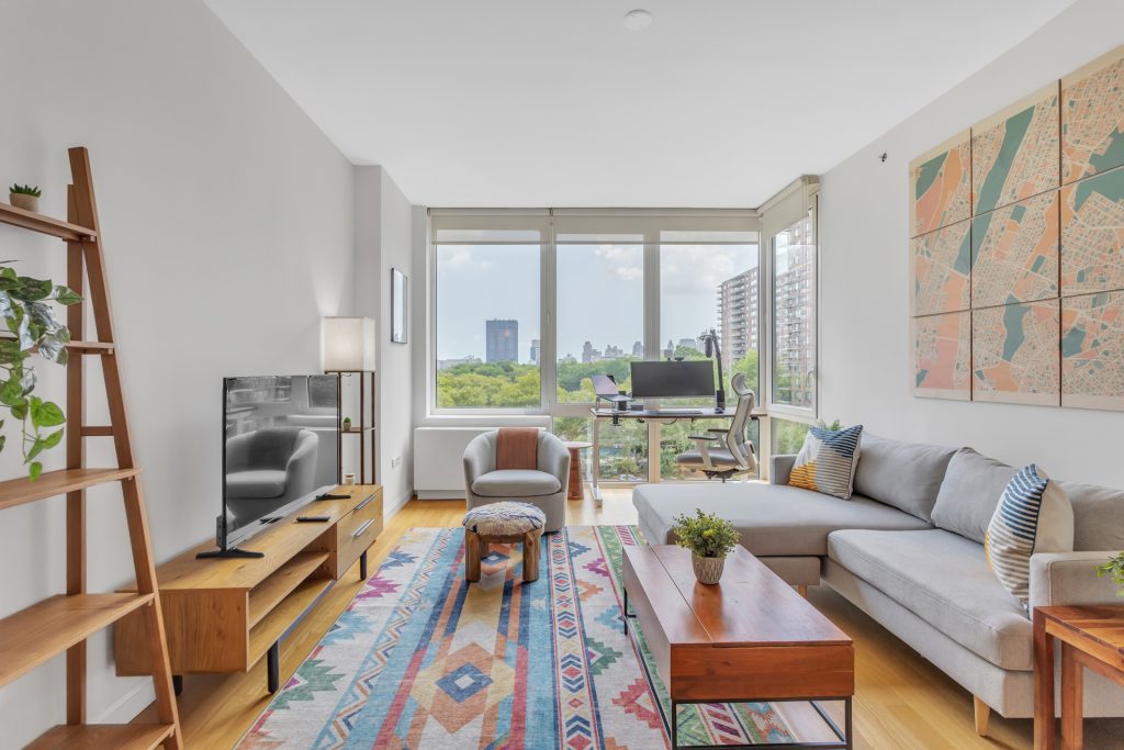 Modern living room with large windows overlooking the upper west side, featuring stylish furniture, colorful rug, and wall art.