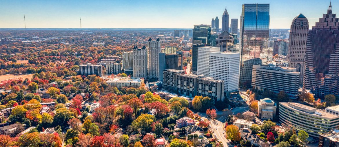 Aerial view of a cityscape with a mix of modern skyscrapers and buildings, surrounded by colorful autumn foliage and a clear blue sky—a perfect setting for any digital nomad.