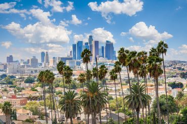 Moving to Los Angeles: Pros, Cons, and Tips for a Seamless Move Downtown Los Angeles skyline with tall buildings and palm trees in the foreground, under a blue sky with scattered clouds.