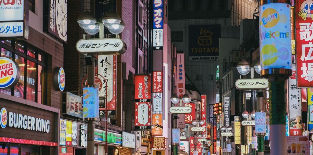 Colorful neon-lit street in Tokyo's busy Shibuya district, crowded with people and shops.