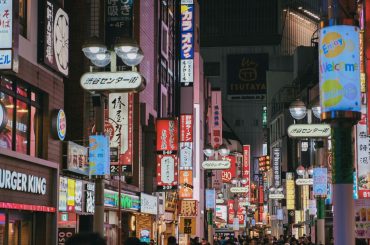 Colorful neon-lit street in Tokyo's busy Shibuya district, crowded with people and shops.