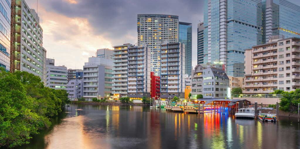 Apartment buildings along a canal in Tokyo at dusk, with lit boats docked on the water