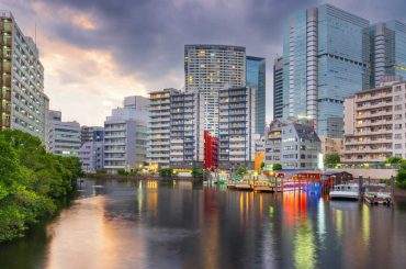 Apartment buildings along a canal in Tokyo at dusk, with lit boats docked on the water